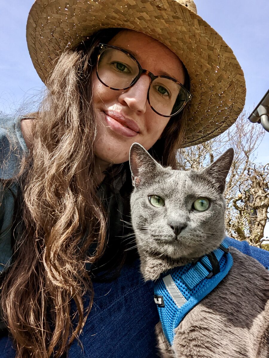 Deborah mit Strohhut und Nala im blauen Geschirr bei einem Ausflug in den Garten